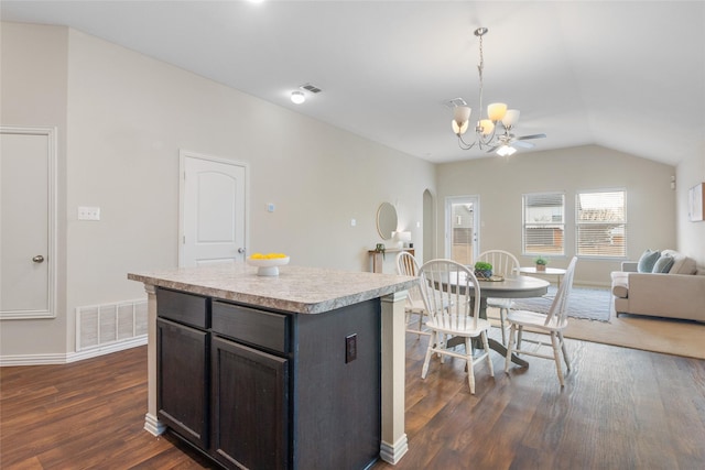 kitchen featuring dark wood-type flooring, lofted ceiling, a kitchen island, pendant lighting, and ceiling fan with notable chandelier