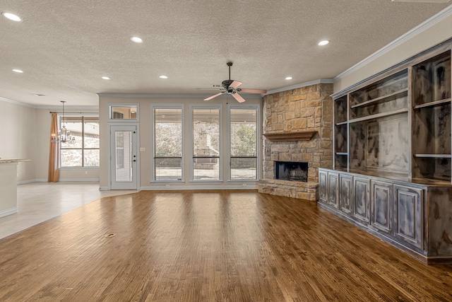 unfurnished living room featuring a textured ceiling, hardwood / wood-style floors, a stone fireplace, ceiling fan, and crown molding