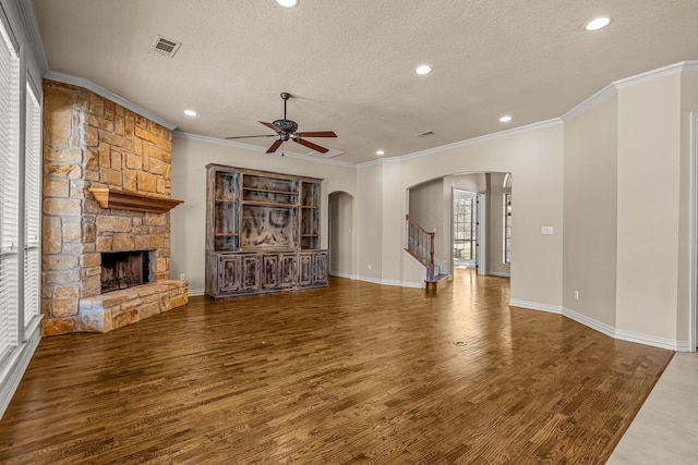 unfurnished living room featuring a textured ceiling, dark wood-type flooring, a fireplace, ornamental molding, and ceiling fan