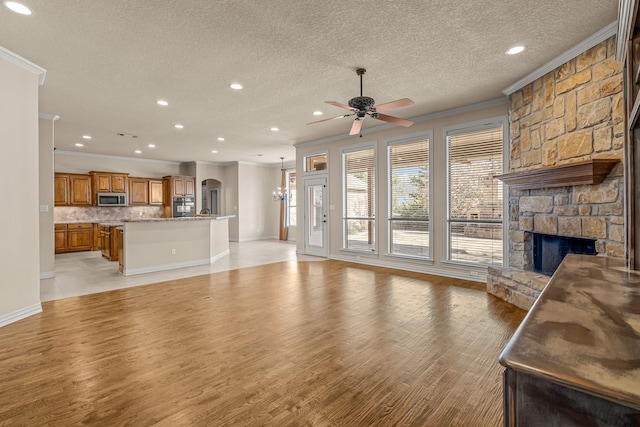 unfurnished living room with ceiling fan, a textured ceiling, crown molding, and a fireplace