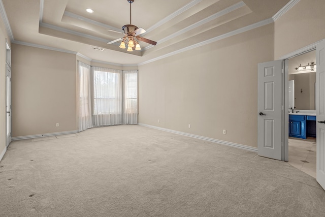 interior space with ceiling fan, a tray ceiling, ensuite bath, light colored carpet, and crown molding