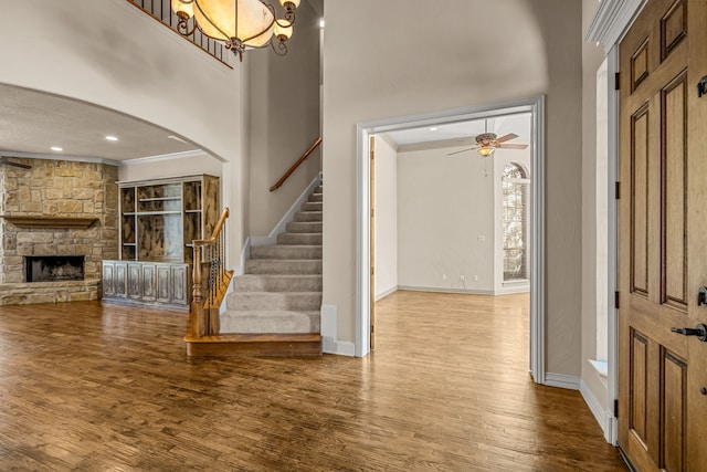 entryway with ceiling fan with notable chandelier, crown molding, a fireplace, and hardwood / wood-style flooring