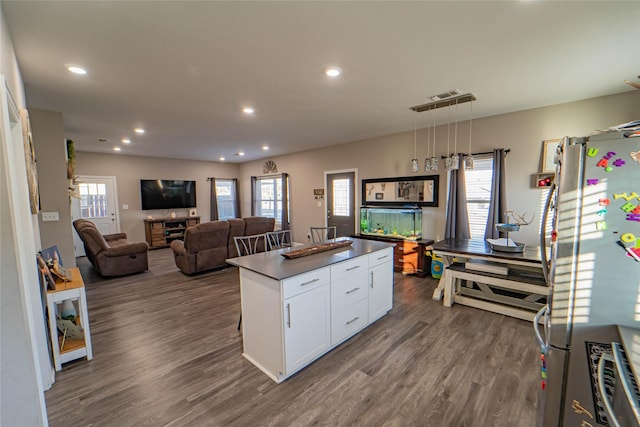 kitchen with white cabinetry, dark wood-type flooring, hanging light fixtures, stainless steel refrigerator, and a kitchen island