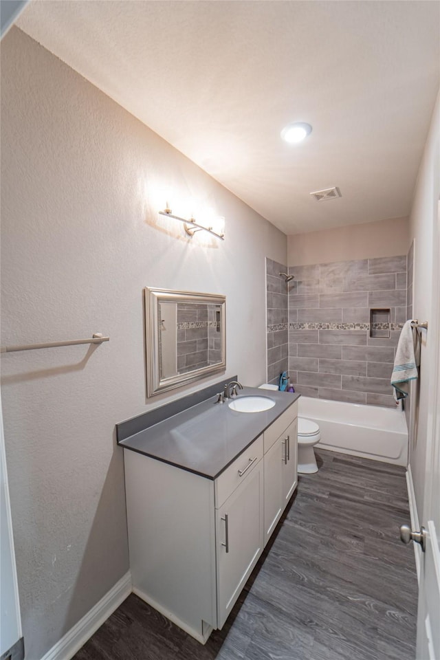 full bathroom with toilet, tiled shower / bath, hardwood / wood-style flooring, and vanity