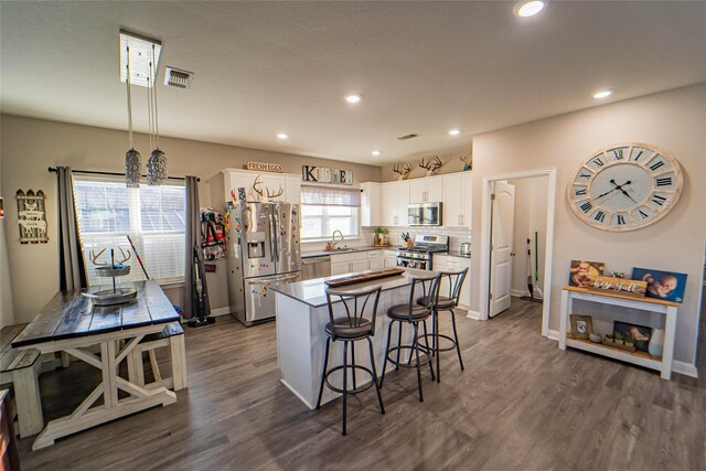 kitchen featuring pendant lighting, a kitchen island, sink, stainless steel appliances, and white cabinets