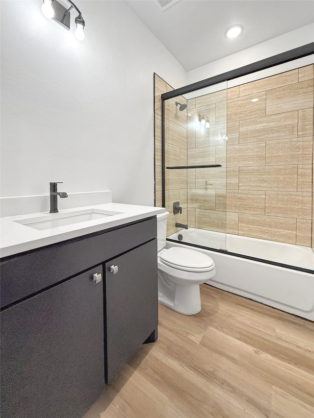 full bathroom with hardwood / wood-style floors, toilet, vanity, and combined bath / shower with glass door