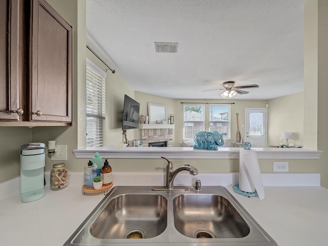 kitchen with ceiling fan, a brick fireplace, sink, and a textured ceiling