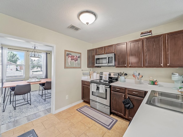 kitchen with appliances with stainless steel finishes, pendant lighting, sink, light tile patterned floors, and a textured ceiling