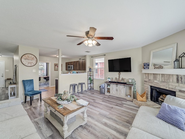 living room featuring ceiling fan, light hardwood / wood-style floors, and a brick fireplace