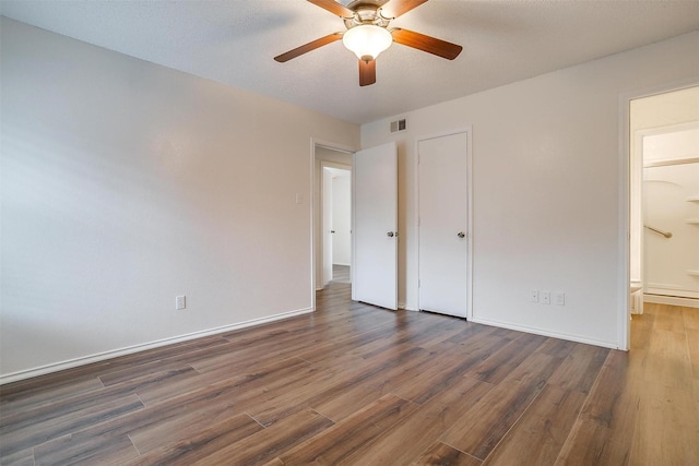 unfurnished bedroom with ceiling fan, ensuite bath, dark hardwood / wood-style floors, and a textured ceiling