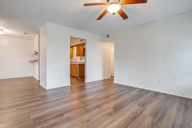 interior space with a textured ceiling, ceiling fan, wood-type flooring, and sink