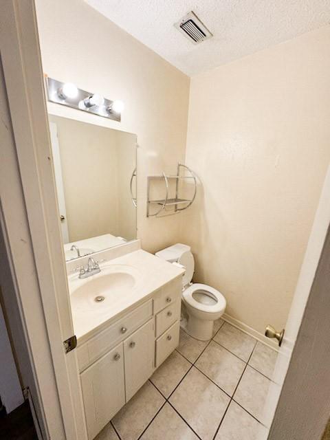 half bathroom featuring tile patterned flooring, vanity, toilet, a textured ceiling, and visible vents