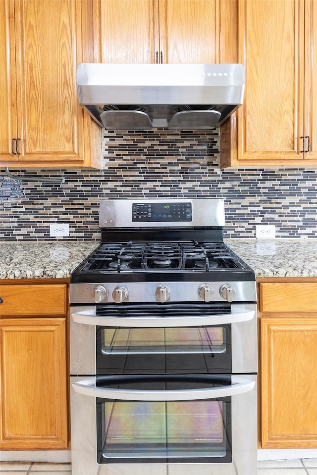 kitchen with light stone counters, double oven range, backsplash, and range hood