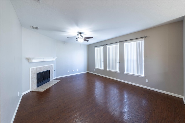 unfurnished living room with ceiling fan, dark wood-type flooring, and a tile fireplace