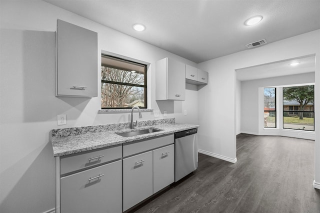 kitchen with a wealth of natural light, stainless steel dishwasher, light stone counters, and sink