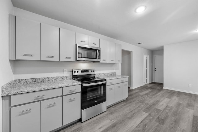 kitchen with light wood-type flooring, appliances with stainless steel finishes, light stone counters, and white cabinetry