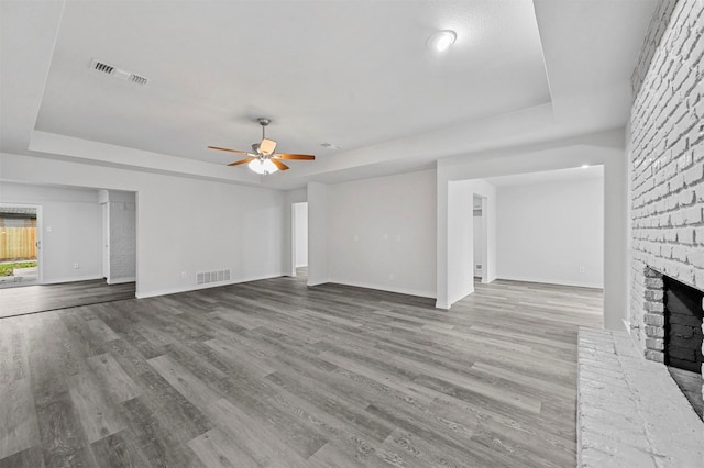 unfurnished living room with ceiling fan, light wood-type flooring, a raised ceiling, and a fireplace