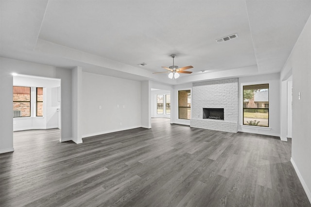 unfurnished living room featuring ceiling fan, a tray ceiling, dark hardwood / wood-style floors, and a fireplace