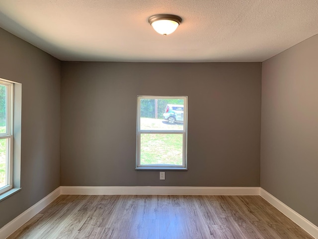 spare room featuring a textured ceiling, a healthy amount of sunlight, and light hardwood / wood-style floors