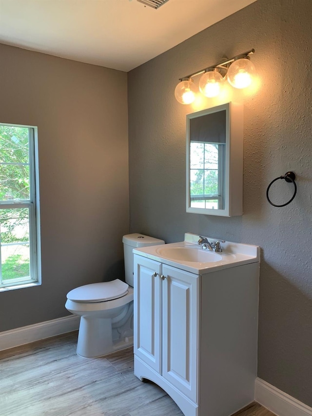 bathroom featuring toilet, vanity, a healthy amount of sunlight, and hardwood / wood-style flooring