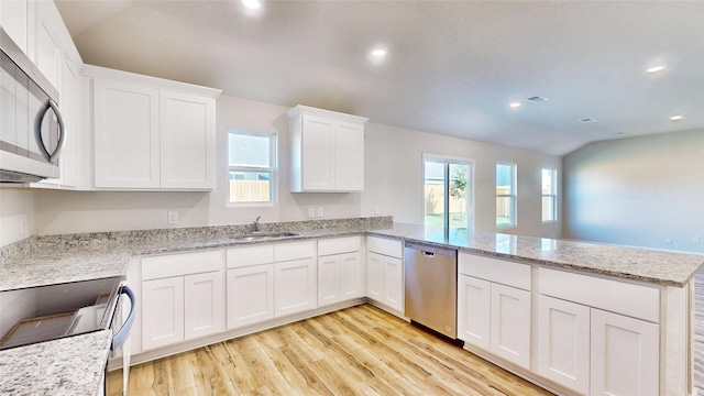 kitchen with kitchen peninsula, appliances with stainless steel finishes, lofted ceiling, white cabinets, and sink