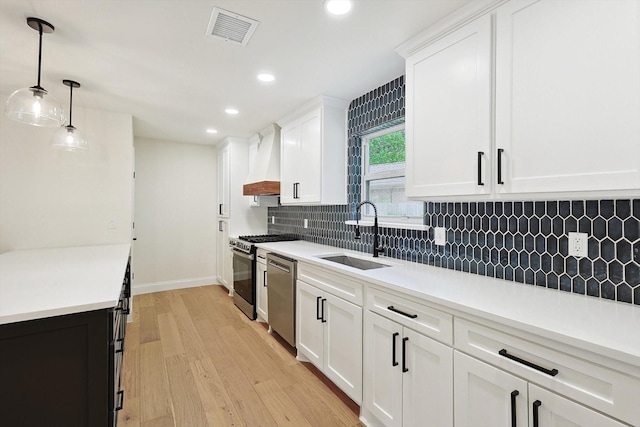 kitchen featuring white cabinetry, custom exhaust hood, stainless steel appliances, decorative light fixtures, and sink