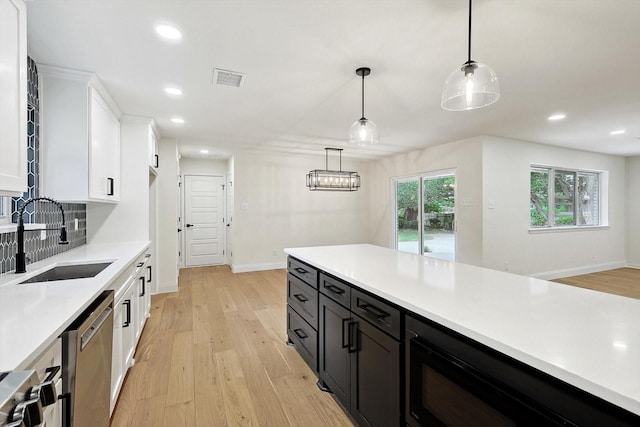 kitchen with stainless steel appliances, white cabinets, pendant lighting, light hardwood / wood-style flooring, and sink