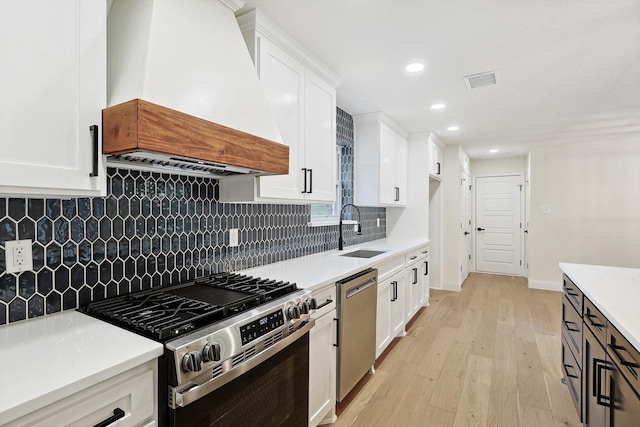 kitchen featuring stainless steel appliances, sink, white cabinets, and custom range hood