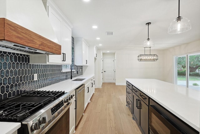 kitchen with pendant lighting, white cabinets, stainless steel appliances, sink, and premium range hood