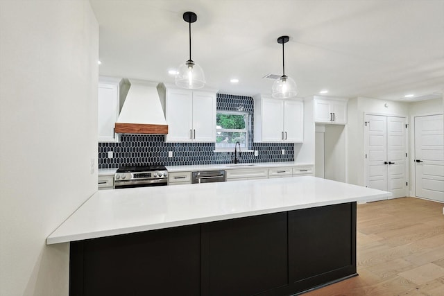 kitchen featuring decorative light fixtures, custom exhaust hood, sink, appliances with stainless steel finishes, and white cabinets