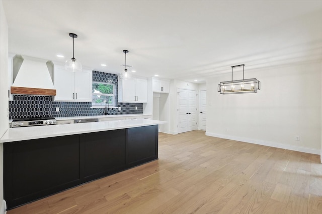 kitchen featuring white cabinetry, decorative light fixtures, light wood-type flooring, stove, and custom range hood