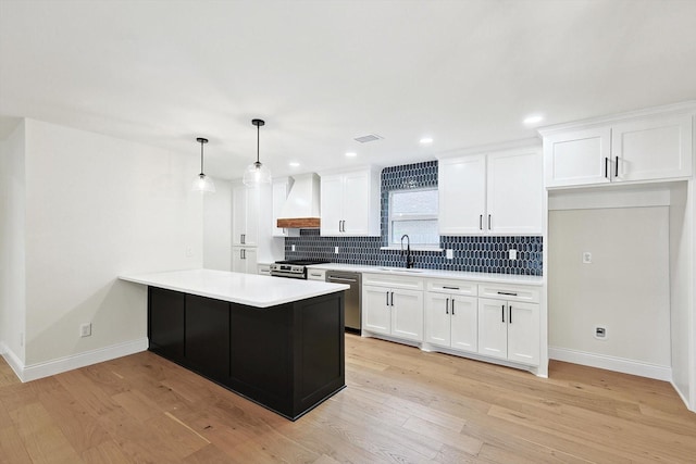 kitchen featuring white cabinets, appliances with stainless steel finishes, decorative light fixtures, light wood-type flooring, and custom range hood