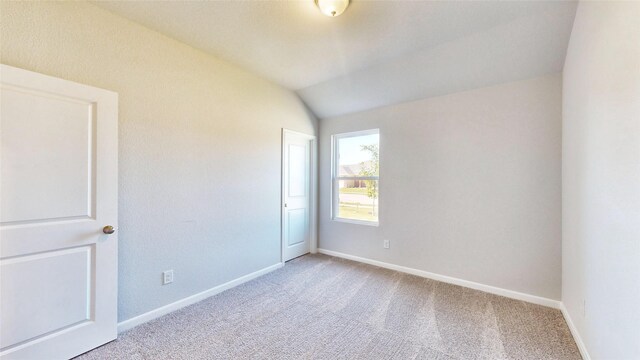 carpeted spare room with vaulted ceiling