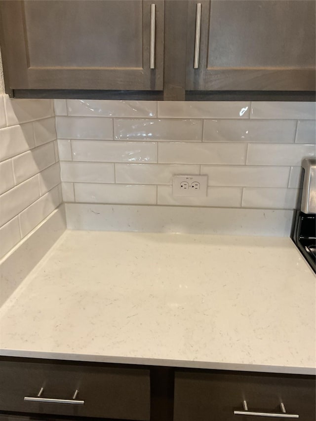 interior details with decorative backsplash, dark brown cabinets, and light stone counters