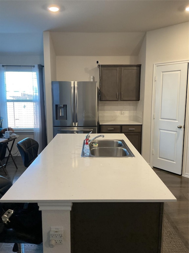 kitchen featuring a center island with sink, stainless steel refrigerator with ice dispenser, backsplash, dark brown cabinets, and sink