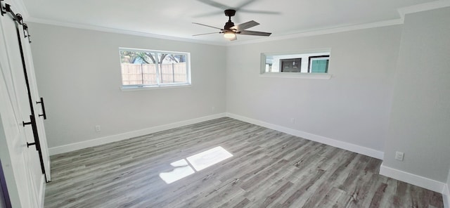 empty room with light wood-type flooring, ceiling fan, crown molding, and a barn door