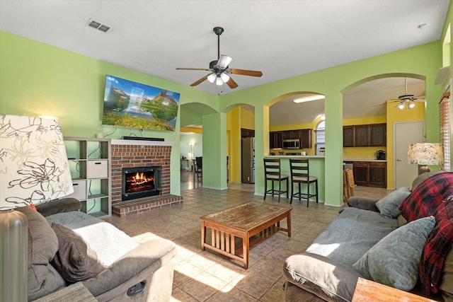 living room with ceiling fan, light tile patterned floors, and a brick fireplace