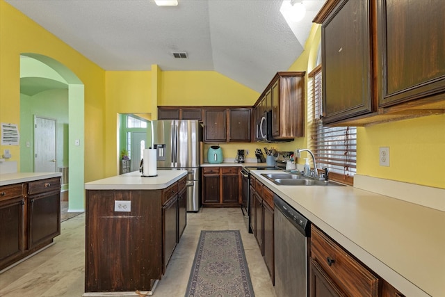 kitchen with stainless steel appliances, vaulted ceiling, a kitchen island, dark brown cabinetry, and sink