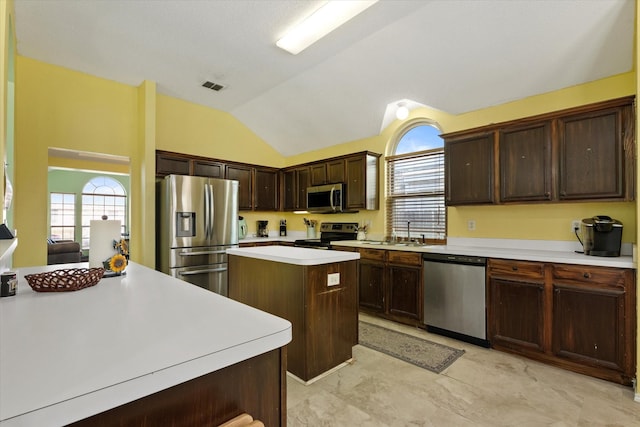 kitchen featuring appliances with stainless steel finishes, a center island, lofted ceiling, dark brown cabinets, and sink