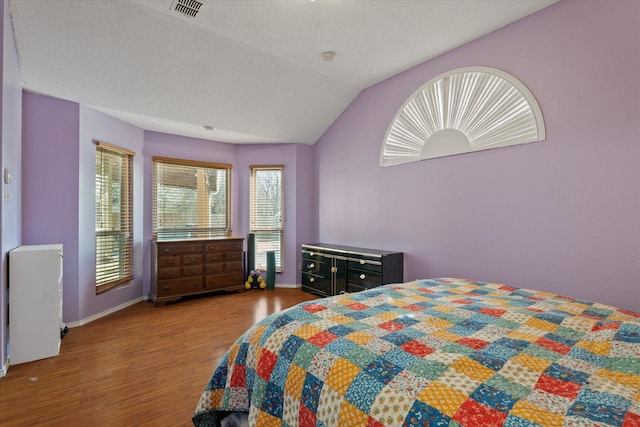 bedroom featuring a textured ceiling, light hardwood / wood-style flooring, and vaulted ceiling