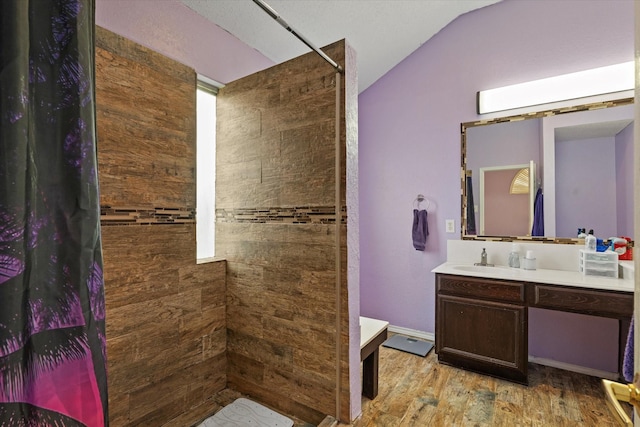 bathroom with lofted ceiling, vanity, hardwood / wood-style flooring, and a tile shower