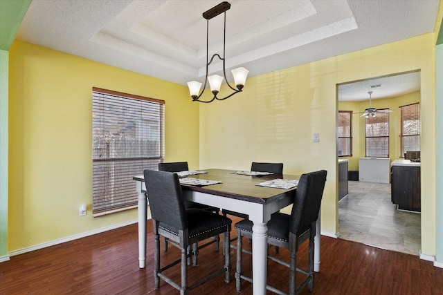 dining space featuring plenty of natural light, ceiling fan with notable chandelier, wood-type flooring, and a tray ceiling