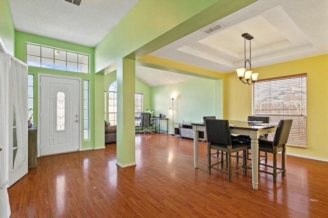 dining area featuring a textured ceiling, hardwood / wood-style flooring, a raised ceiling, and a notable chandelier