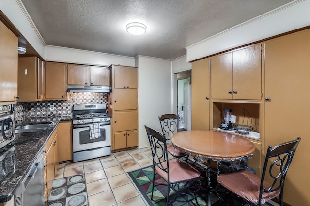 kitchen with a textured ceiling, appliances with stainless steel finishes, dark stone countertops, backsplash, and light tile patterned flooring