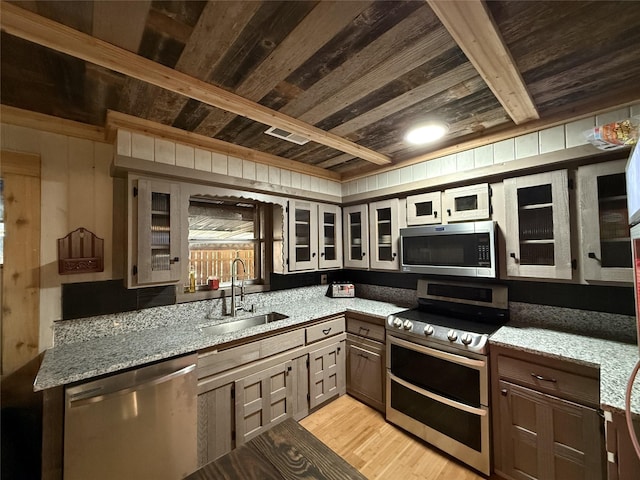 kitchen with appliances with stainless steel finishes, beamed ceiling, light hardwood / wood-style floors, sink, and light stone counters