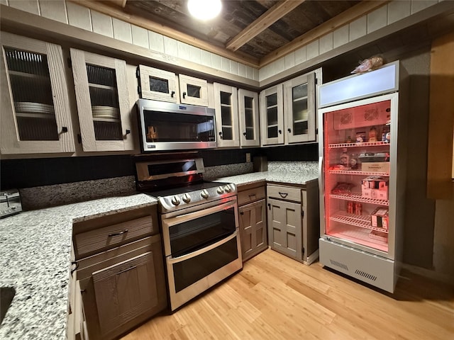 kitchen with light hardwood / wood-style floors, beam ceiling, light stone countertops, appliances with stainless steel finishes, and wooden ceiling