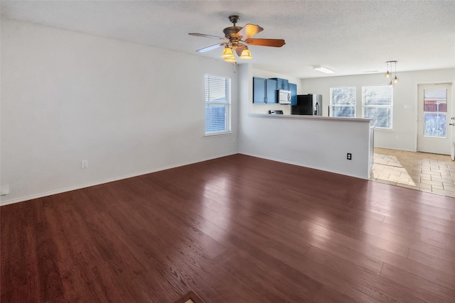 unfurnished living room featuring a textured ceiling, ceiling fan, and dark hardwood / wood-style floors