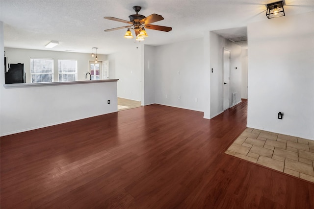 unfurnished living room featuring ceiling fan, dark wood-type flooring, a textured ceiling, and sink