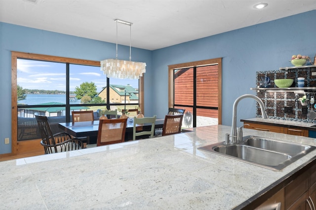 kitchen with sink, a water view, light stone counters, and decorative light fixtures