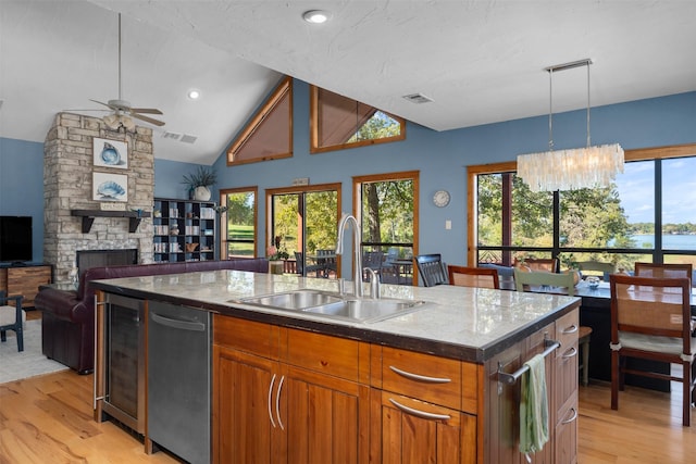 kitchen with an island with sink, decorative light fixtures, light wood-type flooring, wine cooler, and sink